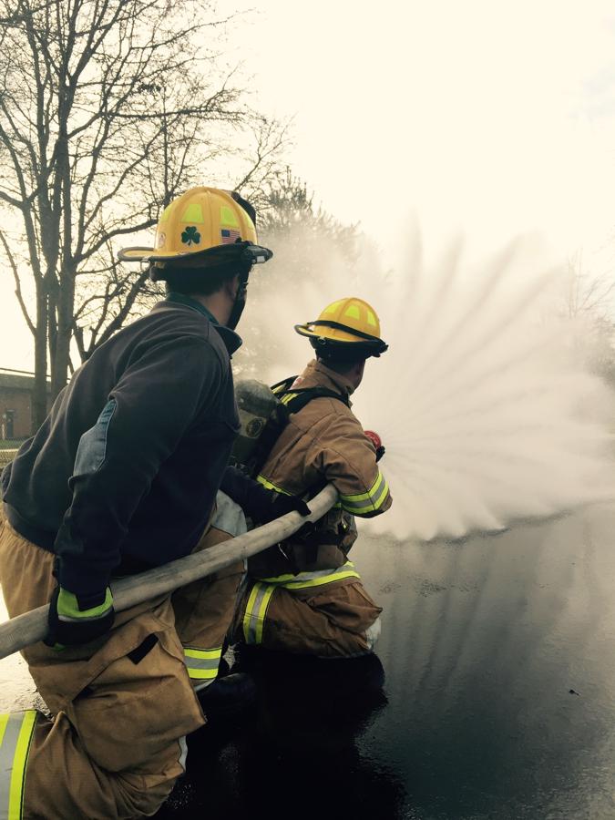 Two trainees advancing a hoseline through smoke during live-fire training