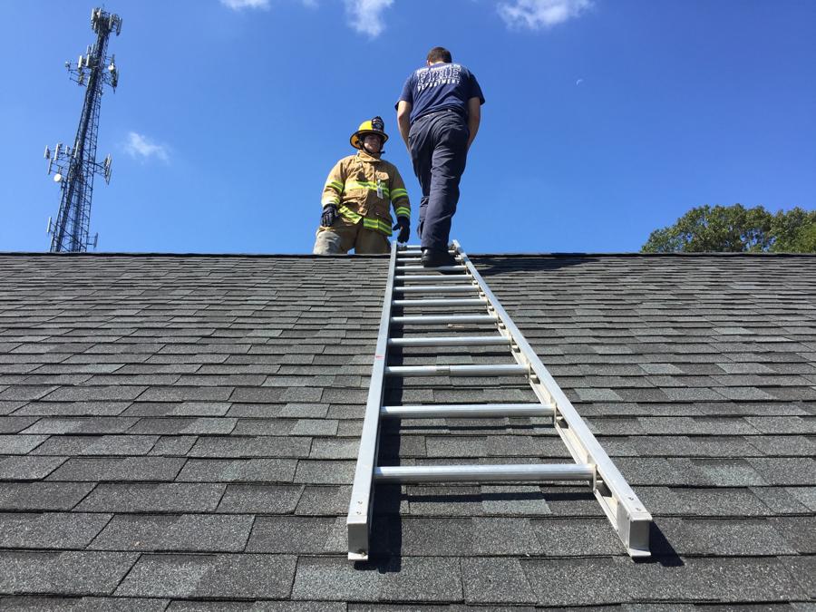 An instructor coaching a new member up a roof ladder on a training building